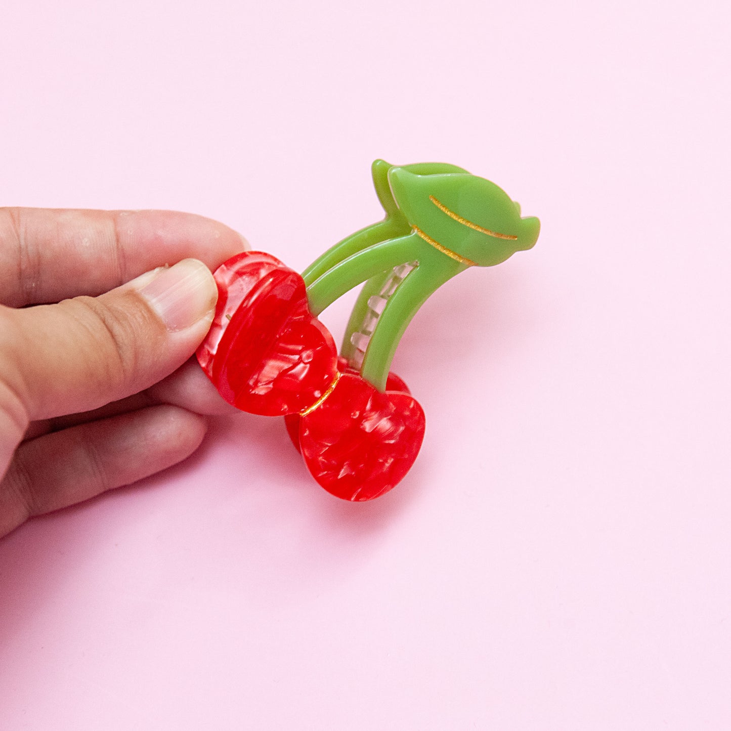 a hand holding a red hair clip in cherry shape