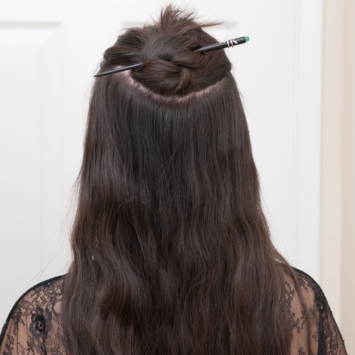 a woman with dark brown hair styled in a half up half down hairstyle, secured with an ebony hair stick featuring a snake design