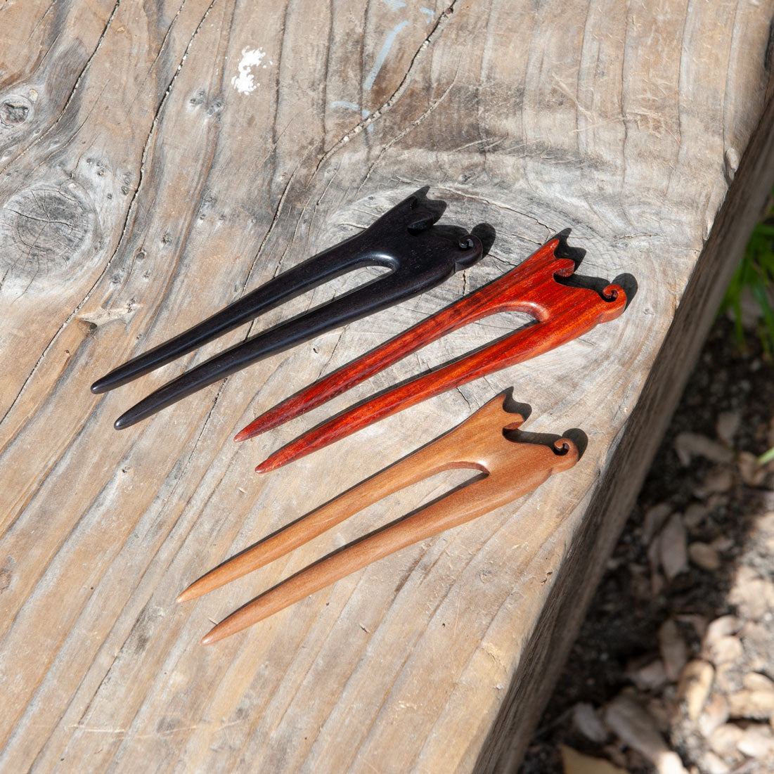 Three cat wooden hair pins in black, red, and natural wood color on a wooden surface.