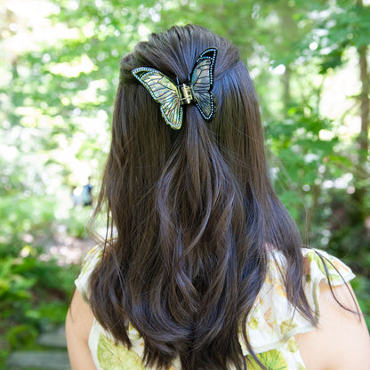 Black butterfly claw clip with iridescent wings styled in a half-up hairstyle.
