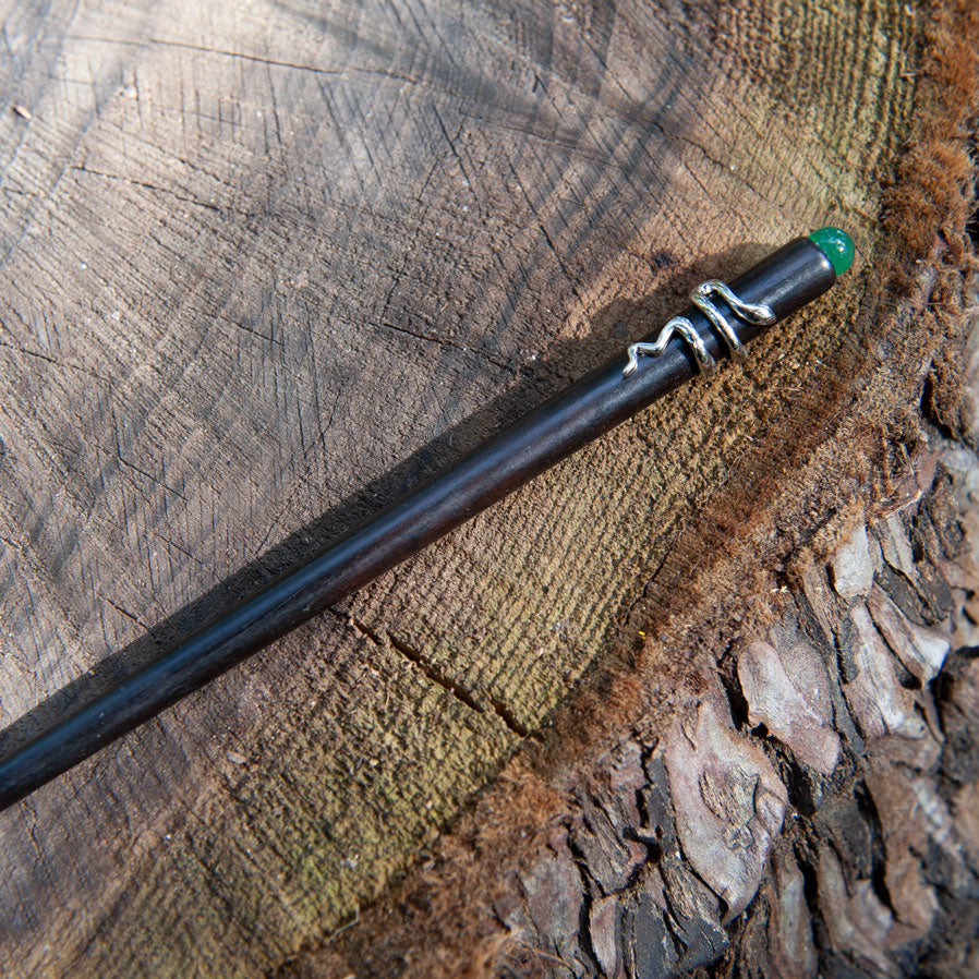 Handmade ebony hair stick with a silver snake coiled around it and a small green bead at the end, elegant and mysterious design.