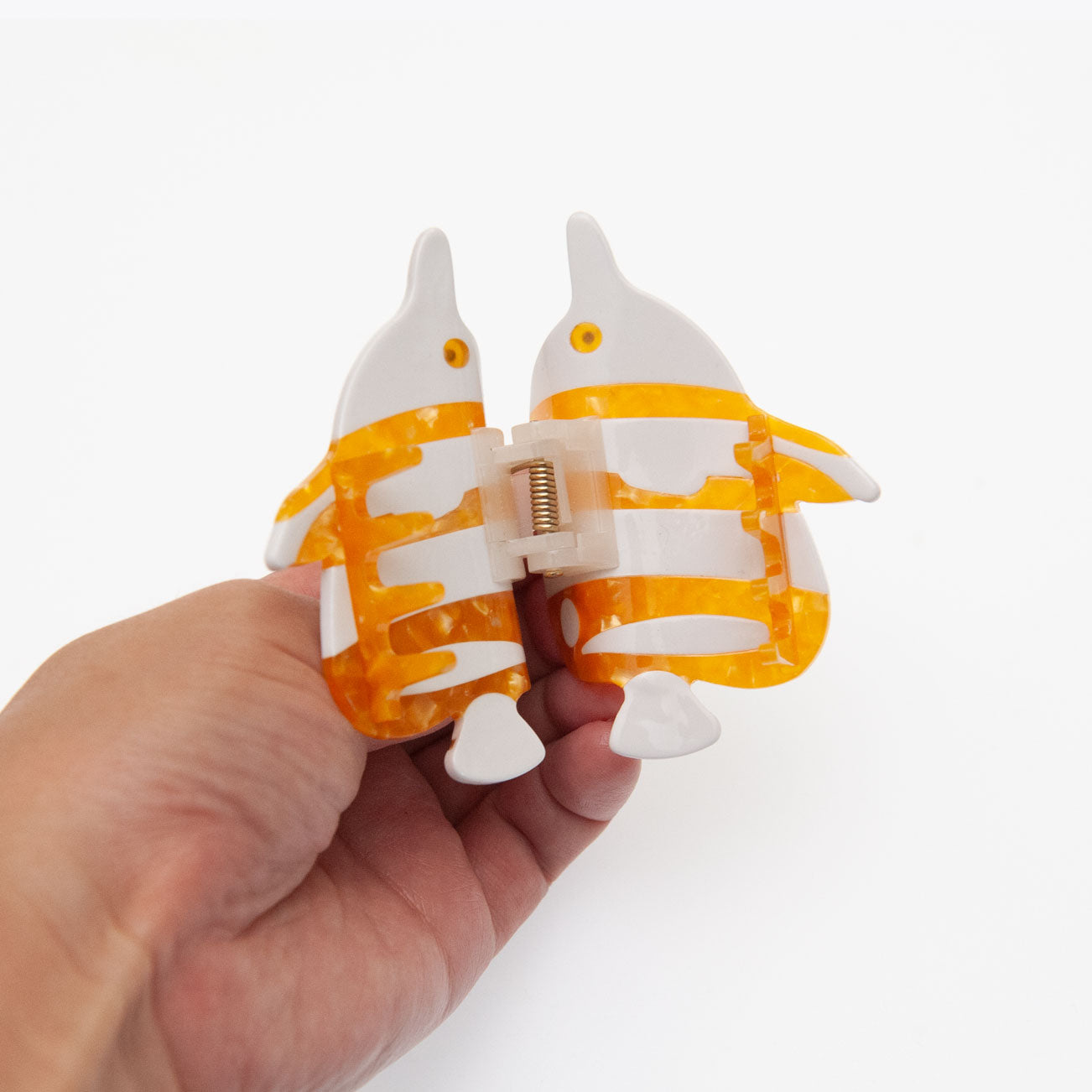 A hand holding a butterflyfish hair claw clip made of translucent orange and white acrylic, shown against a plain white background.
