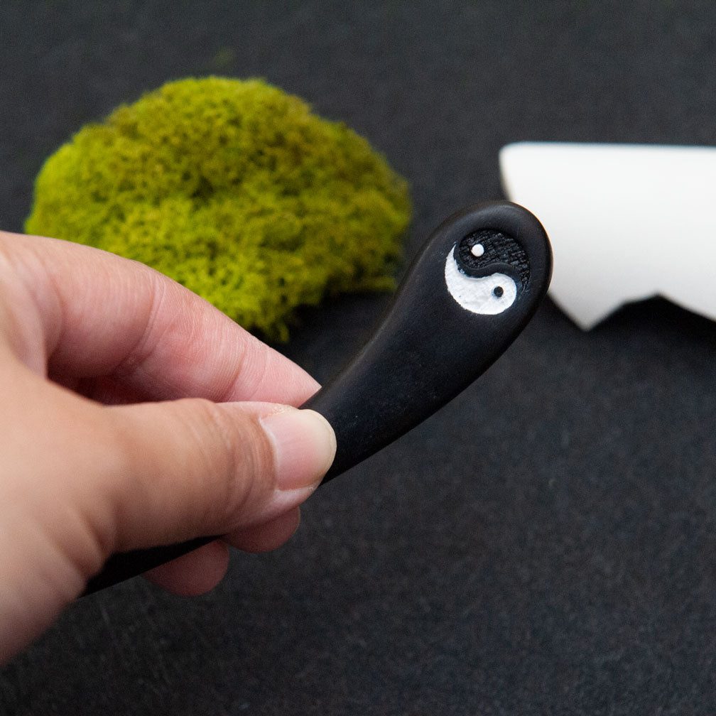 Hand holding a wooden hair stick with a Yin Yang symbol on top