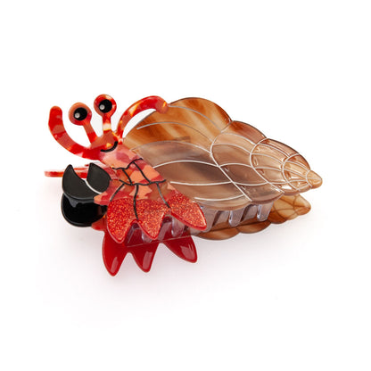 A decorative hair claw clip shaped like a hermit crab, featuring a translucent brown and amber shell, red glittery claws, and black accents, shown on a plain white background.