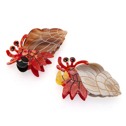 two hermit crab hair clips made of eco-friendly material. One in brown and red, the other one in beige and red.