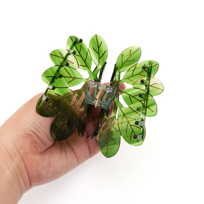 Hand holding a decorative hair clip with leaf design on a white background