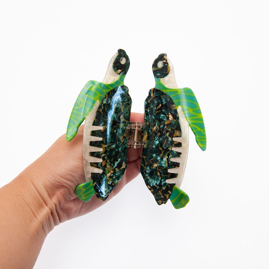 Hand holding a sea turtle claw clip to show its shape and gold details