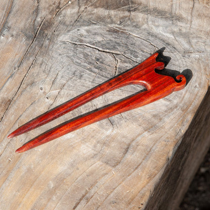 a red padauk wooden cat hair pin with a small cat design and curled tail