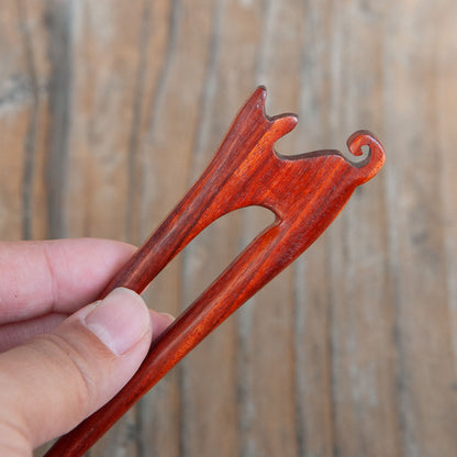 a red padauk wooden cat hair pin with a small cat design and curled tail detail