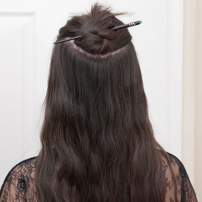 a woman with dark brown hair styled in a half up half down hairstyle, secured with an ebony hair stick featuring a snake design