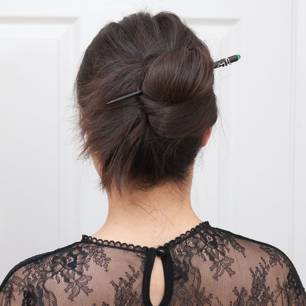 a woman with dark brown hair styled in a full updo bun, secured with an ebony hair stick featuring a snake design