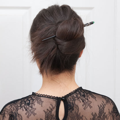 a woman with dark brown hair styled in a full updo bun, secured with an ebony hair stick featuring a snake design