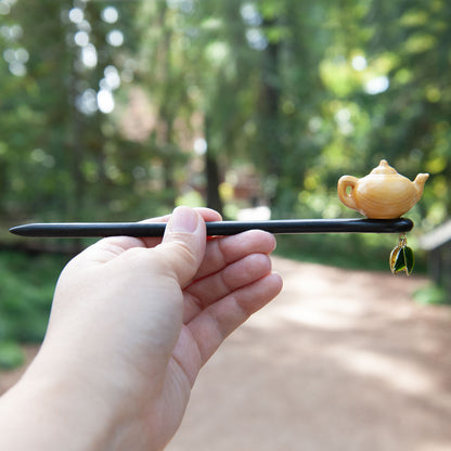 Handmade wooden hair stick featuring a small peach wood teapot and two delicate tea leaves at the end.